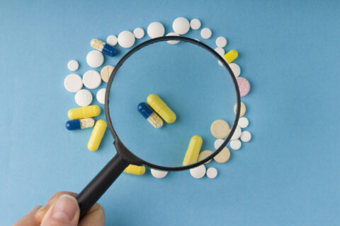 female hand holds a magnifying glass over pills